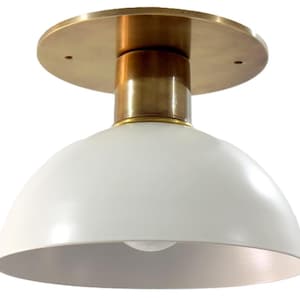 May include: A modern ceiling light fixture with a white, dome-shaped shade and a brass-colored base and stem. The light fixture is designed to be mounted on the ceiling and provides ambient lighting. The fixture is approximately 10 inches in diameter.