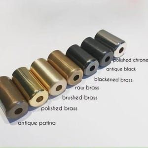 May include: An assortment of cylindrical metal hardware pieces in various finishes, including polished chrome, antique black, and antique patina. The pieces are labeled with their respective finishes, showcasing a range of metallic colors and textures.