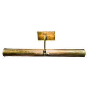 May include: A vintage brass picture light fixture. The fixture has a rectangular backplate, a curved arm, and a long, cylindrical light housing. The brass has a warm, aged patina. The light is designed to be mounted above a picture or artwork.
