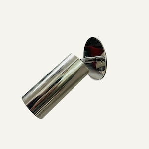 Puede incluir: Una lámpara de pared cromada brillante. El cabezal cilíndrico de la lámpara está en ángulo y conectado a una placa de montaje circular mediante un brazo corto y ajustable. El accesorio refleja el entorno.