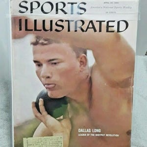 May include: A vintage Sports Illustrated magazine cover from April 25, 1960, featuring Dallas Long, the leader of the shotput revolution. The cover has the magazine's title in large, bold letters. The image shows a man in the act of shot put.