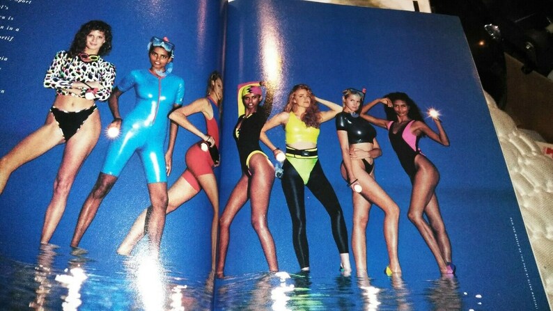 Puede incluir: Siete mujeres con trajes de ba&ntilde;o coloridos posan en una piscina. Las mujeres llevan una variedad de estilos, incluyendo trajes de ba&ntilde;o de una pieza, bikinis y trajes de neopreno. El agua es azul y el fondo es azul brillante.