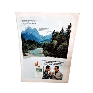 May include: A vintage advertisement for Kool cigarettes featuring a scenic mountain landscape with a river and two men talking. The text reads "Come up to the Kool taste. Taste extra coolness every time you smoke." and "You should have said something sooner. Here, have one of my Kools."
