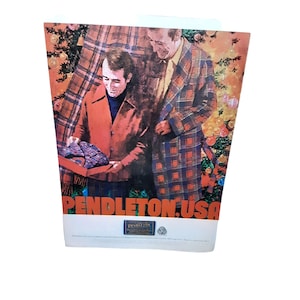 May include: Two men wearing plaid shirts stand in front of a Christmas tree. The man on the left is holding a wrapped gift. The text "PENDLETON.USA" is printed in orange at the bottom of the image.