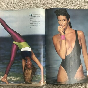 Puede incluir: Dos mujeres con trajes de ba&ntilde;o. Una mujer lleva un traje de ba&ntilde;o negro y est&aacute; de pie en el agua. La otra mujer lleva un traje de ba&ntilde;o rosa y verde y est&aacute; haciendo una pose de yoga en la playa.