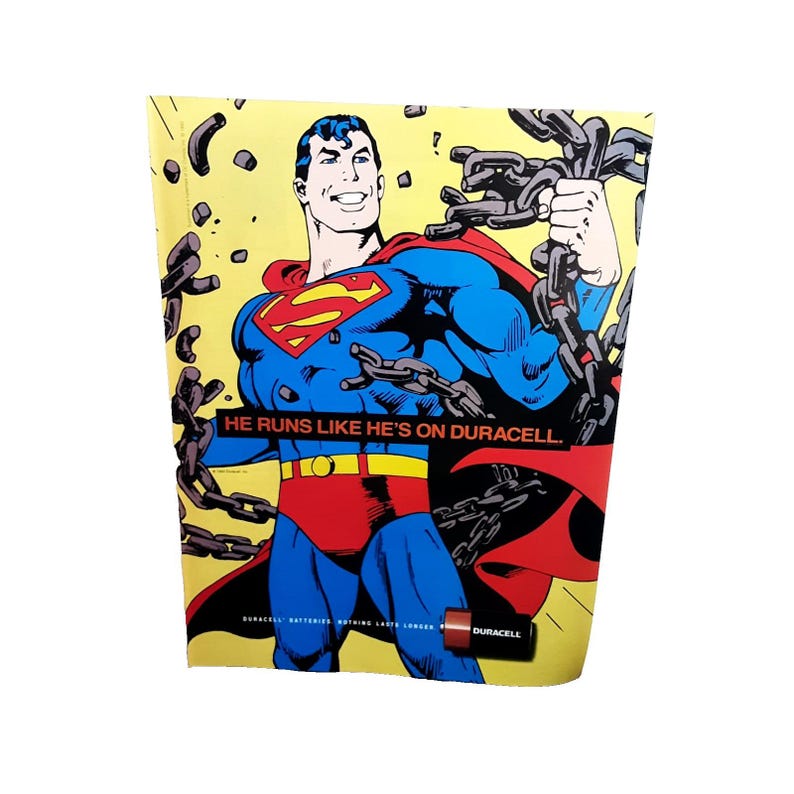 May include: A vintage advertisement featuring Superman in his iconic blue and red suit, breaking chains. The text reads "HE RUNS LIKE HE'S ON DURACELL." A Duracell battery is also visible. The background is yellow.