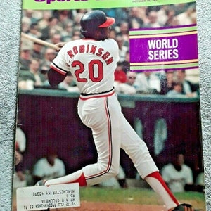 May include: Sports Illustrated magazine cover featuring a baseball player in a red and white uniform with the number 20 and the name "Robinson" on the back. The player is swinging a bat and the text "World Series" is in the upper right corner.