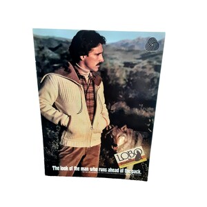 May include: An advertisement featuring a man in a cream-colored zip-up sweater with a brown collar, a plaid shirt, and brown pants. A wolf stands beside him. The text reads, "The look of the man who runs ahead of the pack."