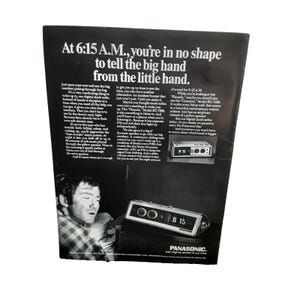May include: Black and white advertisement for a Panasonic digital clock radio. The ad features the text "At 6:15 A.M., you're in no shape to tell the big hand from the little hand." The clock radio displays the time 6:15.