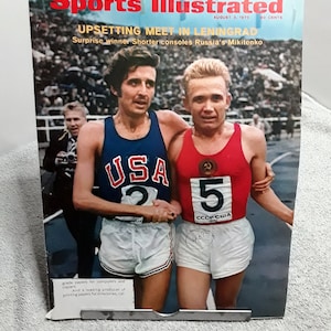 May include: Sports Illustrated magazine cover from August 3, 1970, featuring two runners, one wearing a red and white jersey with the number 5 and the other wearing a blue and white jersey with the number 2. The headline reads "UPSETTING MEET IN LENINGRAD".