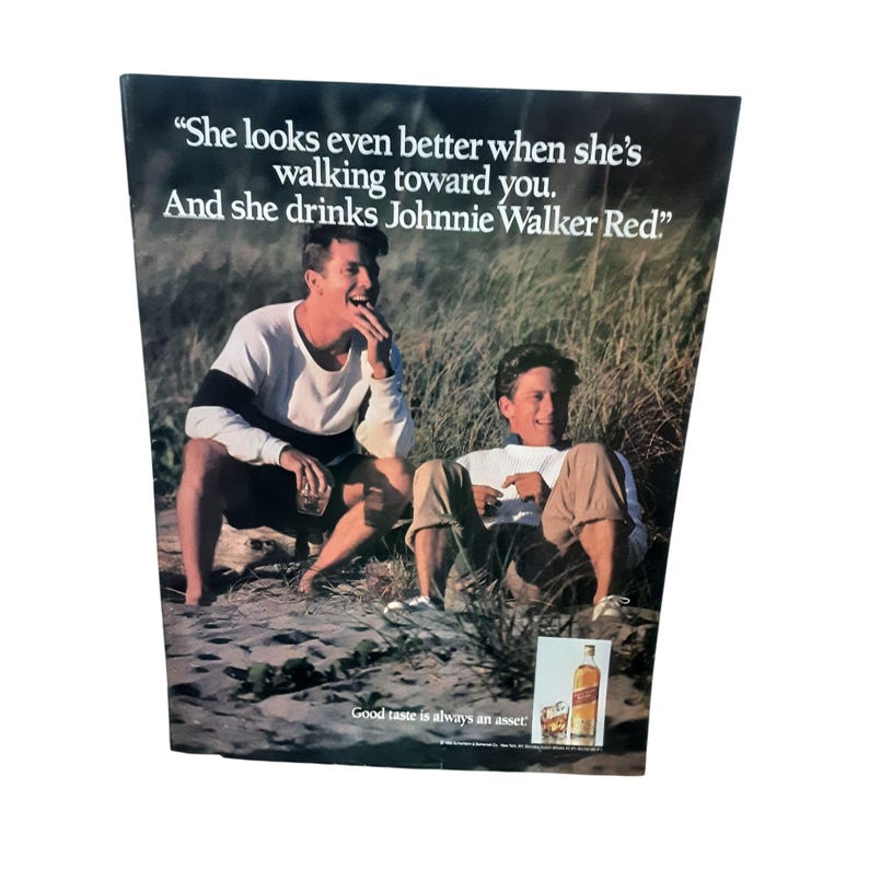 May include: Vintage advertisement featuring two men sitting outdoors, with the text "She looks even better when she's walking toward you. And she drinks Johnnie Walker Red." A bottle of Johnnie Walker Red is visible.