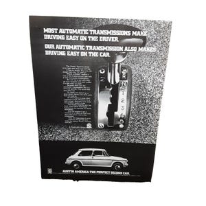 May include: An advertisement for the Austin America car. The ad features a car, a gear shift, and text that reads "MOST AUTOMATIC TRANSMISSIONS MAKE DRIVING EASY ON THE DRIVER." The ad is in black and white.