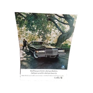 May include: A black Cadillac sedan parked under a large tree with a man walking away from the car. The car has a chrome bumper and a chrome grille. The text "You'll buy your first for what you think it is. And your second for what you know it is." is printed below the car. The text "GM" is printed in the upper right corner of the image. The text "Cadillac" is printed in the lower right corner of the image.