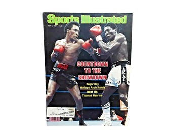 May include: Sports Illustrated magazine cover featuring a boxing match. The cover has the text "Sports Illustrated" in green and the headline "Countdown to the Showdown". Two boxers are shown in action, wearing red gloves and black shorts.