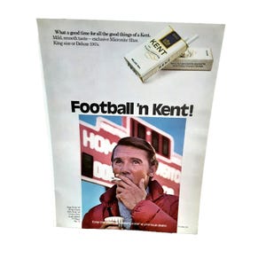 May include: Vintage advertisement for Kent cigarettes. The ad features a man smoking a cigarette, with the text "Football 'n Kent!" and a pack of Kent cigarettes. The ad also includes the text "What a good time for all the good things of a Kent."