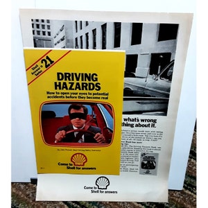 May include: A yellow and black booklet titled "Driving Hazards: How to open your eyes to potential accidents before they become real" by John Pennell, Shell Driving Safety Instructor. The booklet is part of the Shell Answer # Series. The cover features a cartoon illustration of a man driving a red car with a blindfold on. The booklet is advertising a Shell service.
