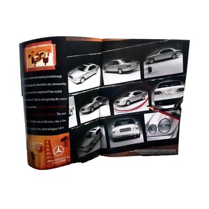 May include: A brochure featuring multiple images of a silver sedan, showcasing different angles and details. The brochure has text that reads "E-Class" and "Road & Track". The brochure is open and displayed against a white background.