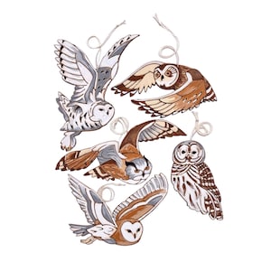 May include: Five wooden owl ornaments painted in shades of brown, white, and gray. The owls are in flight with their wings spread out. Each owl has a string attached to the top for hanging.