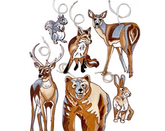 May include: Six wooden ornaments painted with images of forest animals. The ornaments include a deer, a bear, a fox, a rabbit, a squirrel, and a deer. The ornaments are painted in shades of brown, gray, and white.
