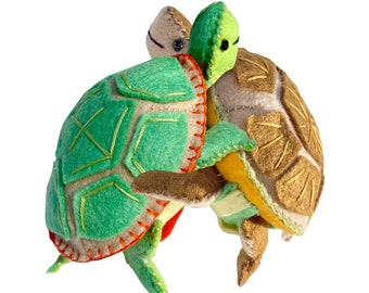 May include: Two felt turtle toys, one green with orange accents and one brown with yellow accents. The turtles are hugging each other.