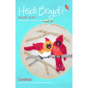 May include: A felt applique embroidery kit featuring two red cardinals perched on a branch. The kit is titled "Cardinal" and includes the text "Quick and easy applique & embroidery kits".