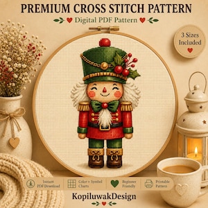 May include: A digital cross stitch pattern featuring a nutcracker in a green hat with red berries, a red jacket, and green trousers. The text reads PREMIUM CROSS STITCH PATTERN, Digital PDF Pattern, 3 Sizes Included, Instant PDF Download, Colour + Symbol Charts, Beginner Friendly, Printable Pattern, and KopiluwakDesign.