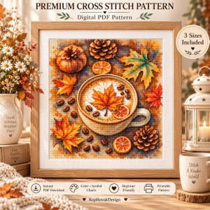 Könnte beinhalten: Ein gerahmtes Kreuzstichmuster mit einer zentralen Kaffeetasse, die mit einem Ahornblatt verziert ist, umgeben von herbstlichen Elementen wie Orangenscheiben, Tannenzapfen und Kaffeebohnen. Der Text lautet Premium Cross Stitch Pattern.