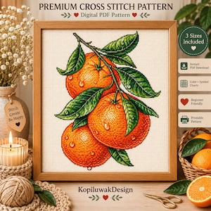 Könnte beinhalten: Ein gerahmtes Kreuzstichmuster mit drei leuchtend orangefarbenen Zitrusfrüchten mit grünen Blättern und Wassertropfen. Das Design wird auf einem weißen Rasterhintergrund mit dem Text Premium Cross Stitch Pattern und KopiluwakDesign gezeigt.