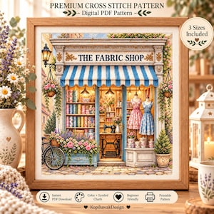 May include: A framed cross stitch pattern titled THE FABRIC SHOP featuring a storefront with a blue and white striped awning, shelves of fabric rolls, a sewing machine, and two mannequins wearing dresses, surrounded by flowers and a bicycle.