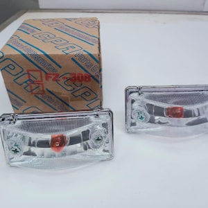 Könnte beinhalten: Zwei transparente rechteckige Leuchten mit roter Mittellinse und silbernen Schrauben. Ein Karton mit der Aufschrift "CPR Accessories Parts & FZ-308" befindet sich im Hintergrund. Fahrzeugteile.