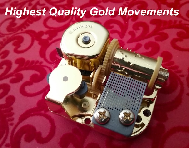 May include: Gold-colored music box movement with a winding key, a comb, and a small metal plate with two screws. The movement is on a red background.