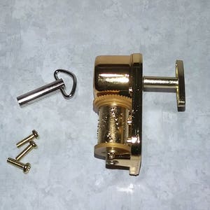 May include: A gold-colored music box mechanism with a winding key and a T-shaped handle. The mechanism is accompanied by a silver-colored winding key and four small gold-colored screws.