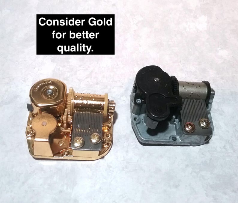 May include: Two music boxes, one gold and one silver, with a black winding key. The gold music box has a gold-colored winding key. The silver music box has a black winding key. The text "Consider Gold for better quality." is visible in the image.