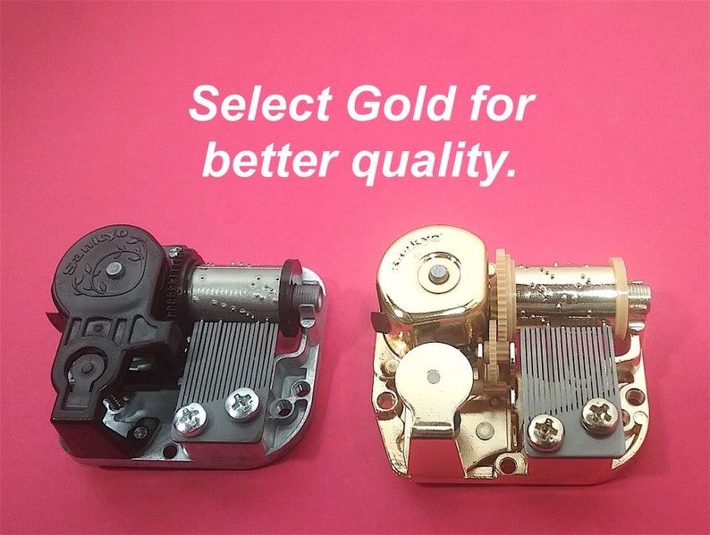 Op de afbeelding: Twee muziekdoosmechanismen, een zwart en een gouden. De tekst "Select Gold for better quality." wordt boven de mechanismen weergegeven.