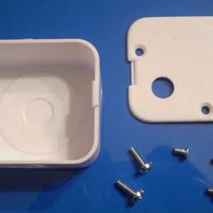May include: A white plastic square box with a round hole in the center and a separate white plastic cover with two round holes. Four silver screws are included.