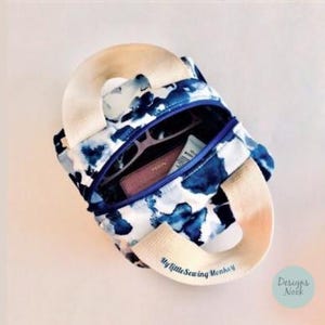 May include: A small, open-top tote bag with a blue and white watercolor pattern. The bag has a zippered pocket containing sunglasses, a wallet, and a tube of cream. The bag has a beige handle and the text "My Little Sewing Menhiey".