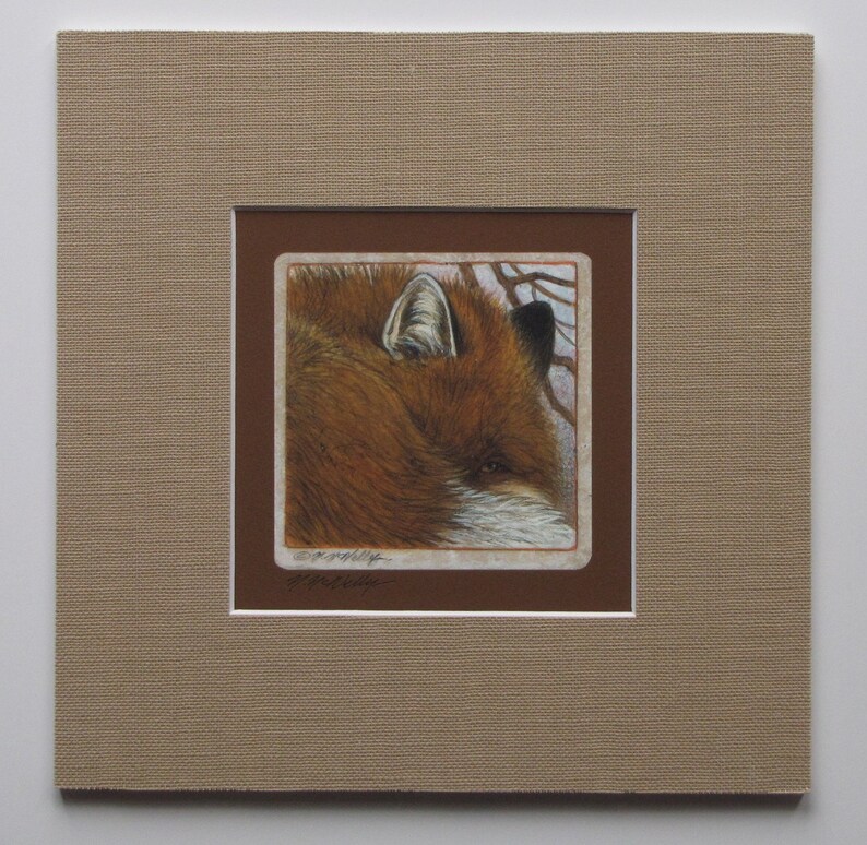 May include: A framed artwork featuring a detailed illustration of a fox's head. The fox has reddish-brown fur, a white muzzle, and a focused gaze. The artwork is matted in brown and framed in a neutral tan color, creating a classic presentation.