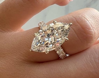 May include: A marquise-cut diamond ring. The large, clear diamond is the focal point, set on a gold band with smaller diamonds. The ring is on a hand with manicured nails.