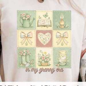 May include: Cream-colored t-shirt featuring a patchwork design with floral and garden-themed illustrations. The design includes a watering can, open book, lamp, bows, heart, boots, basket, and teacups. Text reads "in my granny era".