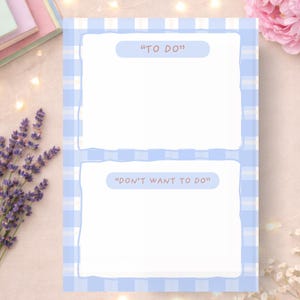 May include: A blue and white gingham patterned notepad with the phrases "TO DO" and "DON'T WANT TO DO" printed on it. The notepad has two blank sections for writing. The image also includes lavender and a pink flower.
