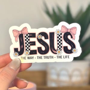 The sticker features the word “JESUS” in bold, playful lettering with a coquette-inspired aesthetic. The design includes pink bows, small daisy flowers, and a trendy checkerboard pattern, giving it a feminine, cute, and modern look. Beneath the main text is the phrase “The Way – The Truth – The Life,” referencing John 14:6.