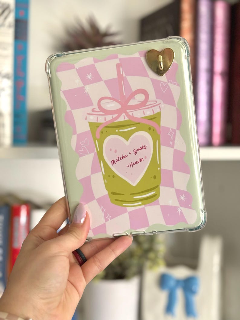 May include: Clear protective case for an e-reader with a green and pink design. The design features a matcha drink illustration with the text "Matcha + Books - Heaven" inside a heart. A gold heart-shaped charm is attached.