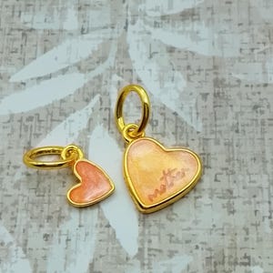 Peut inclure: Deux breloques en forme de cœur doré avec des centres en émail orange clair. La plus grande breloque en forme de cœur porte le mot mother écrit en cursive au centre. Chaque breloque comprend un anneau de jonction doré pour la fixation.