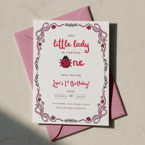 Op de afbeelding: Een witte, rechthoekige verjaardagsuitnodiging met een roze lintrand, kleine rode bloemen en een lieveheersbeestje-afbeelding. De tekst luidt: Our little lady is turning one, join us for Lisa's 1st Birthday, June 12, 1:00 PM, Any House, Any Street, City, RSVP Melissa 12345678.