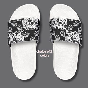 Puede incluir: Dos sandalias deslizantes blancas con un estampado floral en blanco y negro en la parte superior. Las sandalias tienen una plantilla texturizada y el texto "choice of 2 colors".