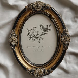 Puede incluir: Un marco de fotos ovalado con acabado dorado y negro. El marco presenta adornos florales y contiene una impresión de dos pájaros posados en una rama con flores. El texto "He is not here; for He is risen. Matthew 28:6" está impreso debajo.