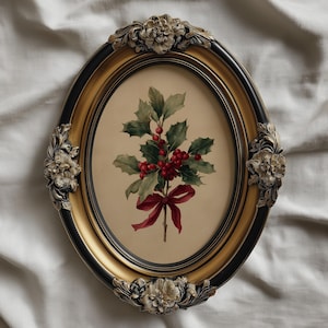 May include: An oval picture frame with a black and gold finish. The frame has floral detailing and contains a botanical print of holly with red berries and a red ribbon. The frame is displayed on white fabric.