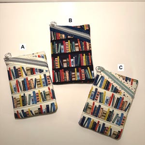 May include: Three rectangular zippered pouches with a quilted book pattern. The pouches are in white, black, and off-white. Each pouch has a silver zipper and a book-themed fabric design with various book spines in different colors.