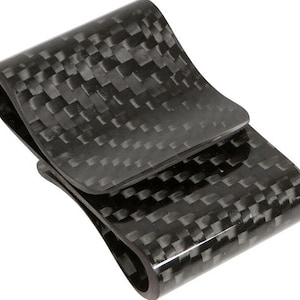 May include: A black carbon fiber money clip with a woven pattern. The clip has a curved design and a spring-loaded mechanism to hold cash and cards securely. The material has a glossy finish.