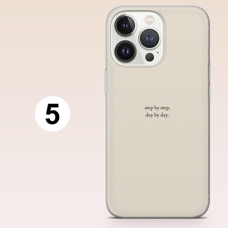 May include: A beige phone case with a clear border. The case has a triple-lens camera cutout and the words "step by step, day by day" in a minimalist font. A white circle with the number 5 is in the upper left corner.